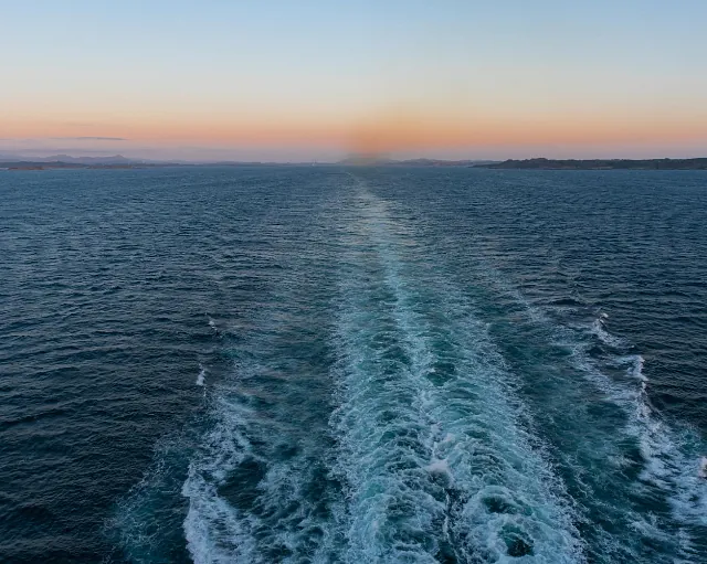 Bølger og kjølvann fra skip i solnedgang, med rolig hav og svakt lys i horisonten.